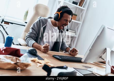So angry! Furious young man in casual clothing using computer and shouting while spending time at home Stock Photo