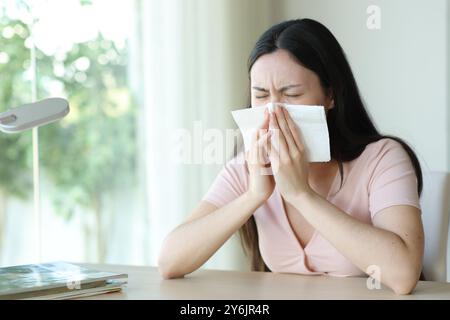 Asian ill woman blowing on tissue sitting at home Stock Photo