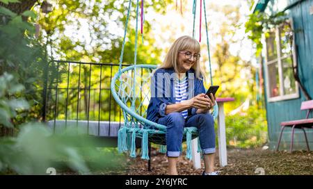 Mature woman using mobile phone while sitting on a swing in the garden Stock Photo
