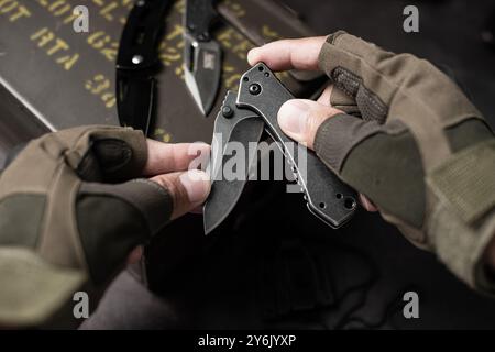 The man wearing tactical gloves using folding knife. Stock Photo