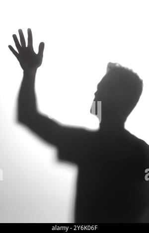 Shadowed silhouette of a man with raised hand, high contrast black and white abstract shot, white background with soft shadows Stock Photo