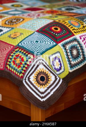 Fragment of a vintage granny squares crochet in many colors and motifs on the wooden bed. Indoor interior concept. Copy space. Stock Photo