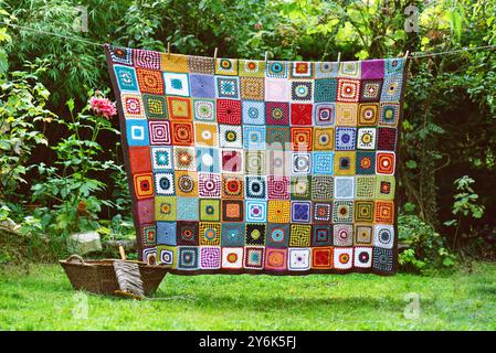 Vintage crochet blanket made from cotton granny squares hanging outdoors on the string with rustic laundry wicker basket. Stock Photo