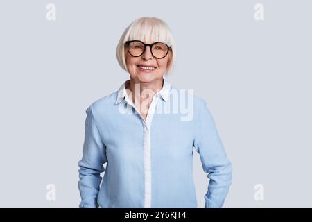 Mature expert. Beautiful senior woman looking at camera and smiling while standing against grey background Stock Photo