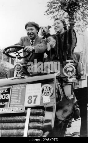 London: In his element at the wheel of a 1903 Cadillac is stage and screen comedian George Formby. with his wife, Beryl, and their pet dog, Punch, George was taking the car out for a trial run to-day in readiness for the London-Brighton Rally on November 1 in which he will drive the Cadillac. 29 October 1953 Stock Photo