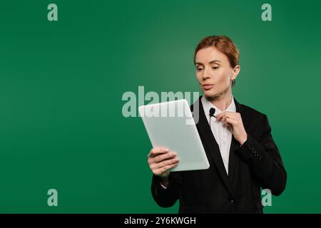 The presenter in elegant black formal attire interacts with viewers while holding a tablet, showcasing charisma. Stock Photo