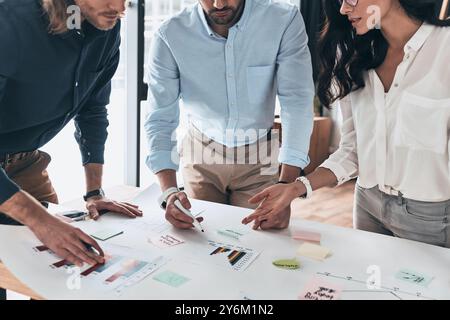 Developing new strategy. Close up of young confident business people communicating together while working with blueprint in the office Stock Photo
