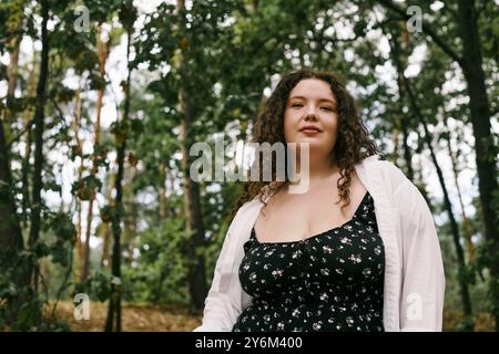 A confident plus size woman stands in a vibrant field surrounded by greenery, embracing nature. Stock Photo