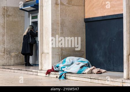 France, Nantes, 44, outside the Grande Poste, woman withdrawing money from an ATM next to a homeless man lying under a blanket, March 2023. Stock Photo