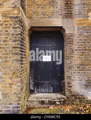 Black door with an arrow pointing left with brick walls around in North London. Stock Photo