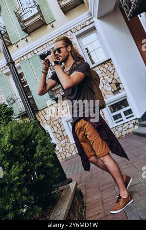 Capturing the moment. Full length of handsome young man in casual clothing photographing something while standing outdoors Stock Photo