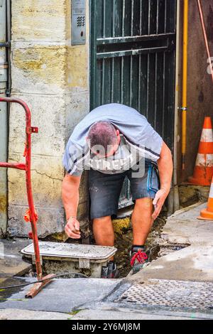 Worker wearing shorts bending down looking at repair work in hole in ground - Tours, Indre-et-Loire (37), France. Stock Photo