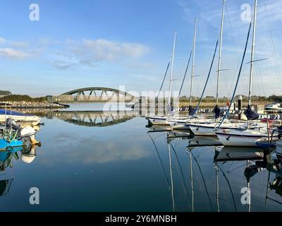 A small railway bridge spans part of Poole harbour on the south coast of England with sailing boats and craft moored in the calm water. Stock Photo
