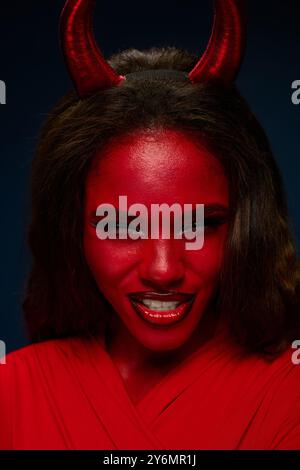 A captivating woman wearing a red costume with horns showcases her playful spirit at Halloween. Stock Photo