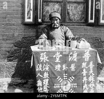 One constant factor in changing China: daily life--typical scenes. A street fortune teller at his table, counting his divining sticks and awaiting custom: an occupation combined with medicine selling as a 'side line'.  27 August 1927 Stock Photo