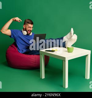 Online shopping activity. Easy and convenient purchases. Young bearded man making orders via laptop, against green studio background Stock Photo
