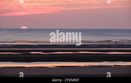 Tranquil sunset over tidal flats with silhouettes of distant figures and reflections on water. Stock Photo