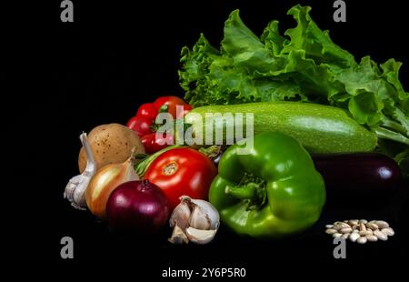 A vibrant assortment of fresh organic vegetables, including lettuce, tomato, pepper, garlic, and zucchini, displayed on a black background, symbolizin Stock Photo