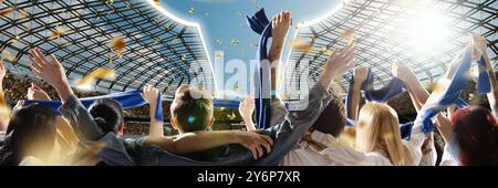 Fans dressed in blue scarves celebrate under sunlit sky, with gold confetti falling around them, while stadium's roof gleams in background. Stock Photo