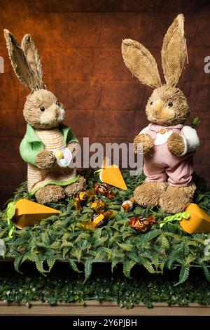 Two stuffed rabbits are sitting on a green carpet with carrots and chocolates in front of them Stock Photo