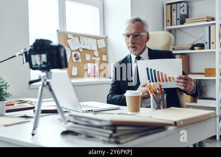 Senior man in elegant business suit showing chart while making social media video Stock Photo