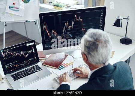 Top rear view of senior trader in elegant business suit using computer while working at the office Stock Photo