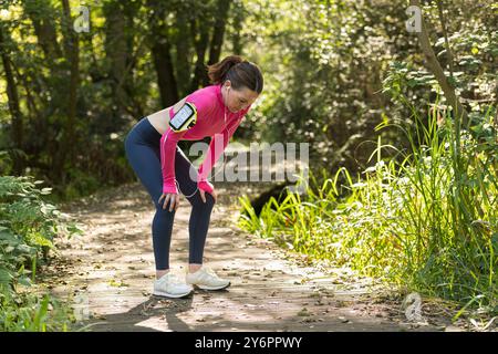 Sporty woman runner with her hands on her knees resting after exercise outdoors. Catching her breath. Stock Photo