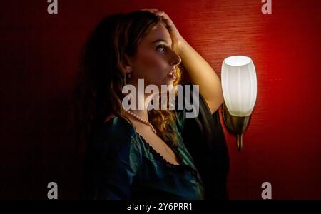 Lovely female model Ava Nicholson sits beside a bright bedside light inside a bedroom at the Dundee Queens Hotel posing for photographs in Scotland Stock Photo