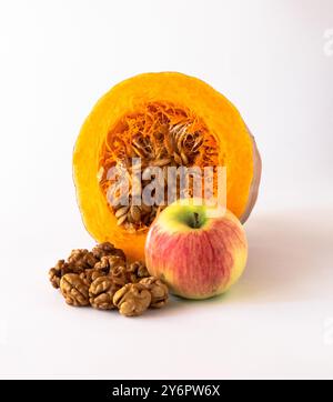 Cut pumpkin with seeds inside, apple, walnut kernels on a white background. Stock Photo