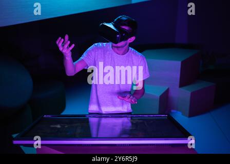 Young man interacting in a digital world, using virtual reality headset with motion tracking tech, making hand gestures in the air. Stock Photo