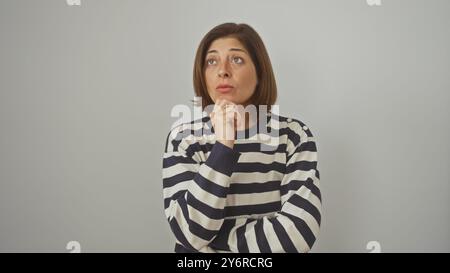 A pensive hispanic middle-aged woman in a striped sweater stands against a white isolated background. Stock Photo
