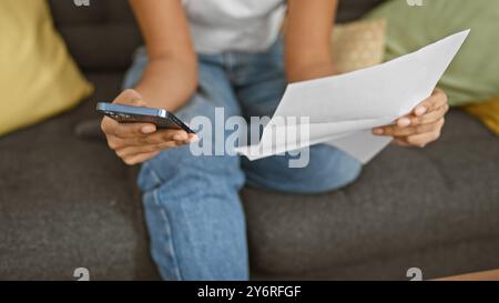 African american woman reading paper and using smartphone indoors Stock Photo