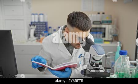 A young bearded man studies specimens under a microscope in an equipped laboratory setting. Stock Photo