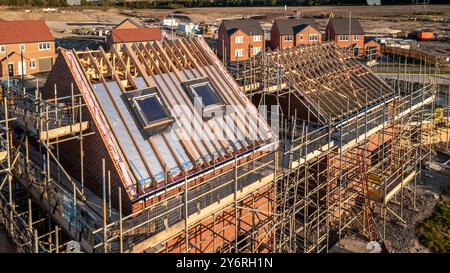 Aerial view of a roof under construction with beams and apex supporting exterior skylight windows on a new build house surrounded by scaffolding on a Stock Photo