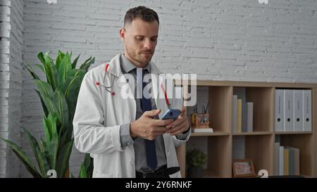 A professional hispanic man in a white coat uses a smartphone in a modern clinic office, symbolizing healthcare technology. Stock Photo
