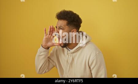 Black man in hoodie shouting against a yellow background, capturing emotions, casual clothing, and sound expression. Stock Photo