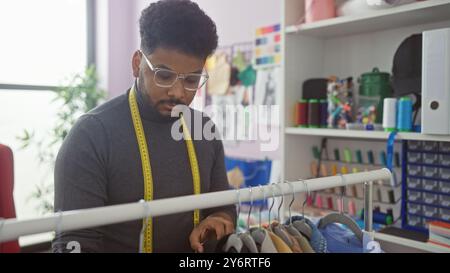 African american man with glasses in a tailor shop browsing fabric swatches, displaying creativity and concentration. Stock Photo