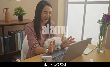 Hispanic woman laughing with white bichon maltes dog at home office Stock Photo