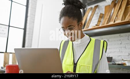 African woman in safety vest using laptop in a modern carpentry workshop Stock Photo