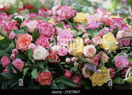 a funeral wreath of orange, pink, yellow and white roses and a white ribbon lies on a fresh grave in a cemetery Stock Photo