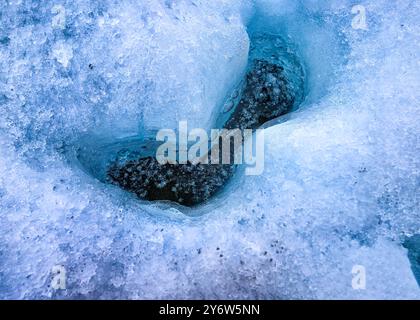 Air bubbles lie trapped in water under a thin layer of ice in a hole in the Glacial blue ice of the Matanuska Glacier Stock Photo