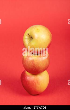 Three Fresh Red and Yellow Apples on Vibrant Red Background – Isolated, Healthy Fruit, and Nutrition Concept Stock Photo