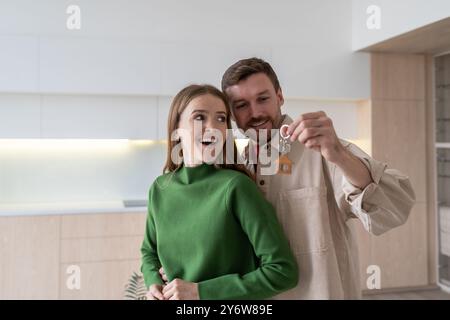Moving house of young family. Excited couple embracing, celebrating with keys after relocation Stock Photo