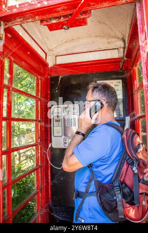 Man chatting talking using a telephone in an traditional red English telephone box kiosk design  no 6  / K6 designed in 1935 by Sir Gilbert Scott Stock Photo