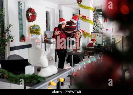 Focused employees working on tough project on Christmas season. Diverse business coworkers brainstorming and analyzing statistics during winter holidays in festive decorated office Stock Photo