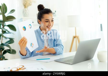 Virtual business meeting. Successful indian or arabian woman, company ceo, sit at workplace with laptop, having online business meeting with coworkers, doing presentation by video call with client Stock Photo
