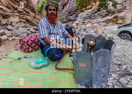 WADI LAJAB, SAUDI ARABIA - NOVEMBER 25, 2021: Local man wearing a traditional floral headpiece making coffee in Wadi Lajab canyon, Saudi Arabia Stock Photo