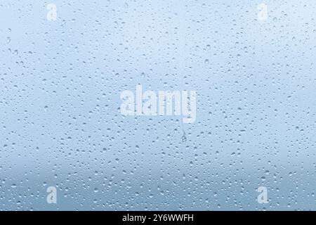 Raindrops collect on the surface of a window, creating a soft, blurry effect that obscures the view outside on a cloudy afternoon in early fall. Stock Photo