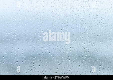 Raindrops accumulate on a window, obscuring the view and creating a tranquil ambiance on a gray, overcast day, suggesting peaceful solitude indoors. Stock Photo