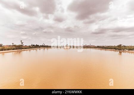 View across the reservoir at Menara Gardens, with cloudy sky and water, palm trees and pavilion in the background, Moroccan architecture, Marrakech, M Stock Photo